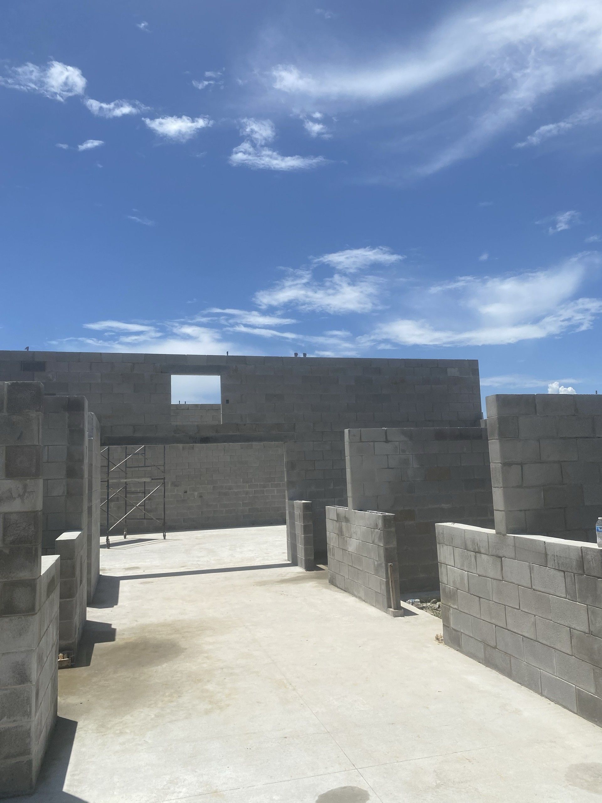 Interior concrete block partition walls with framed door openings and vertical rebar inside a roofless building shell under a blue sky