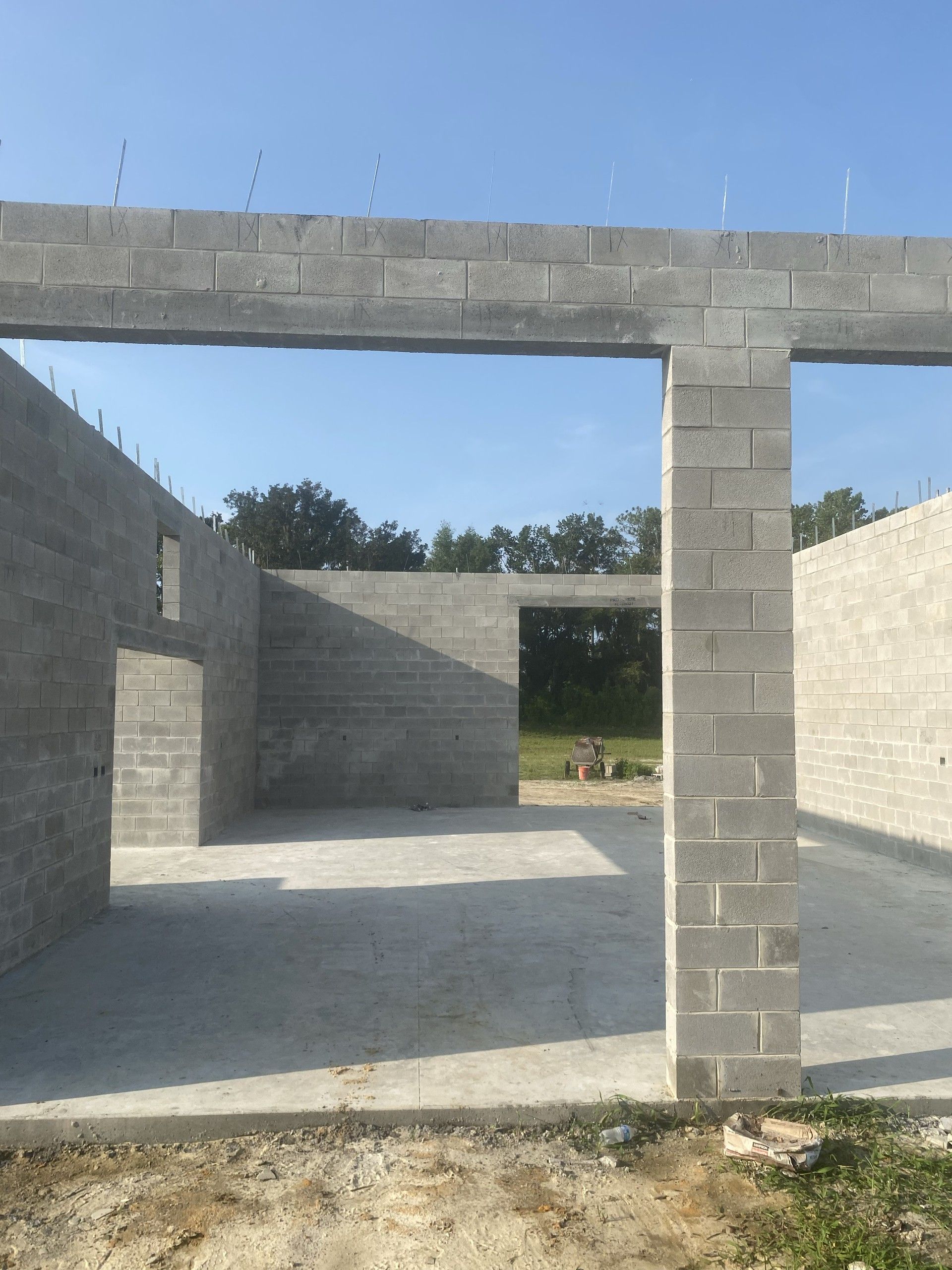 A wide opening in a concrete block wall spanned by a bond beam, with a reinforced block pilaster at one side and open sky above