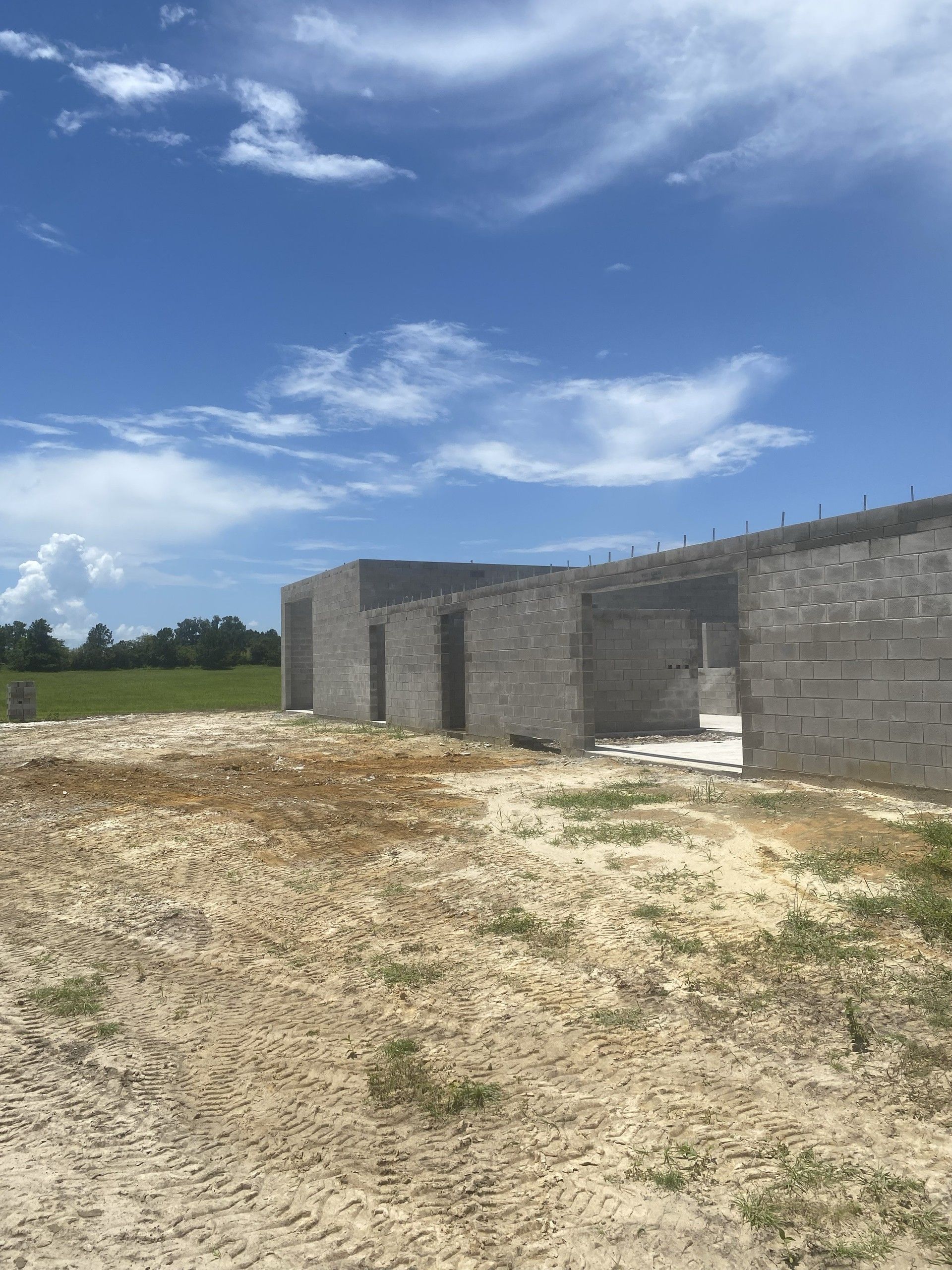 Clean concrete block walls of a large building shell rise against a bright blue sky, with green pasture and fencing visible beyond the openings