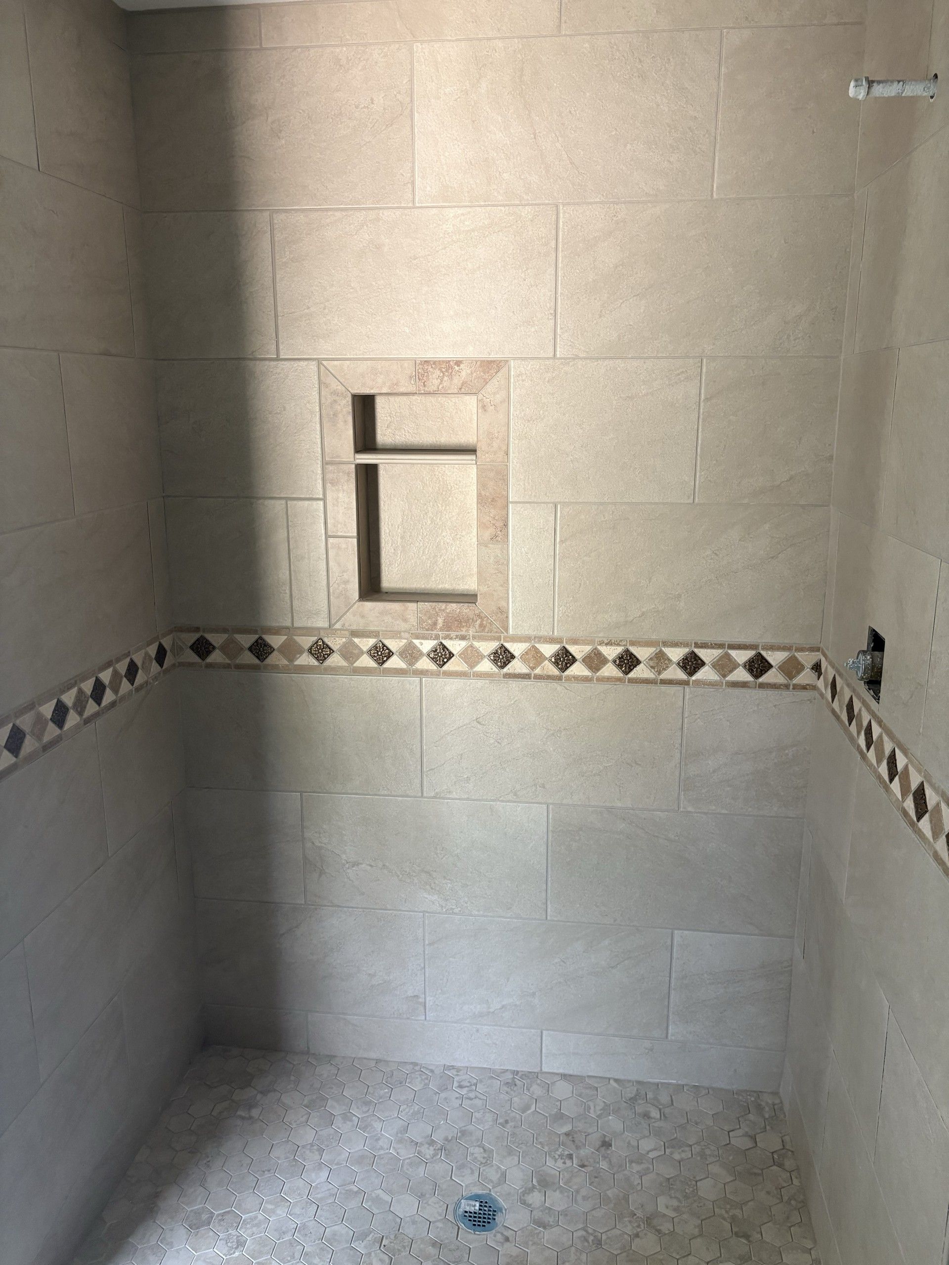 Tiled shower stall with a recessed shelf niche, decorative tile border, and hexagonal mosaic floor tile with drain