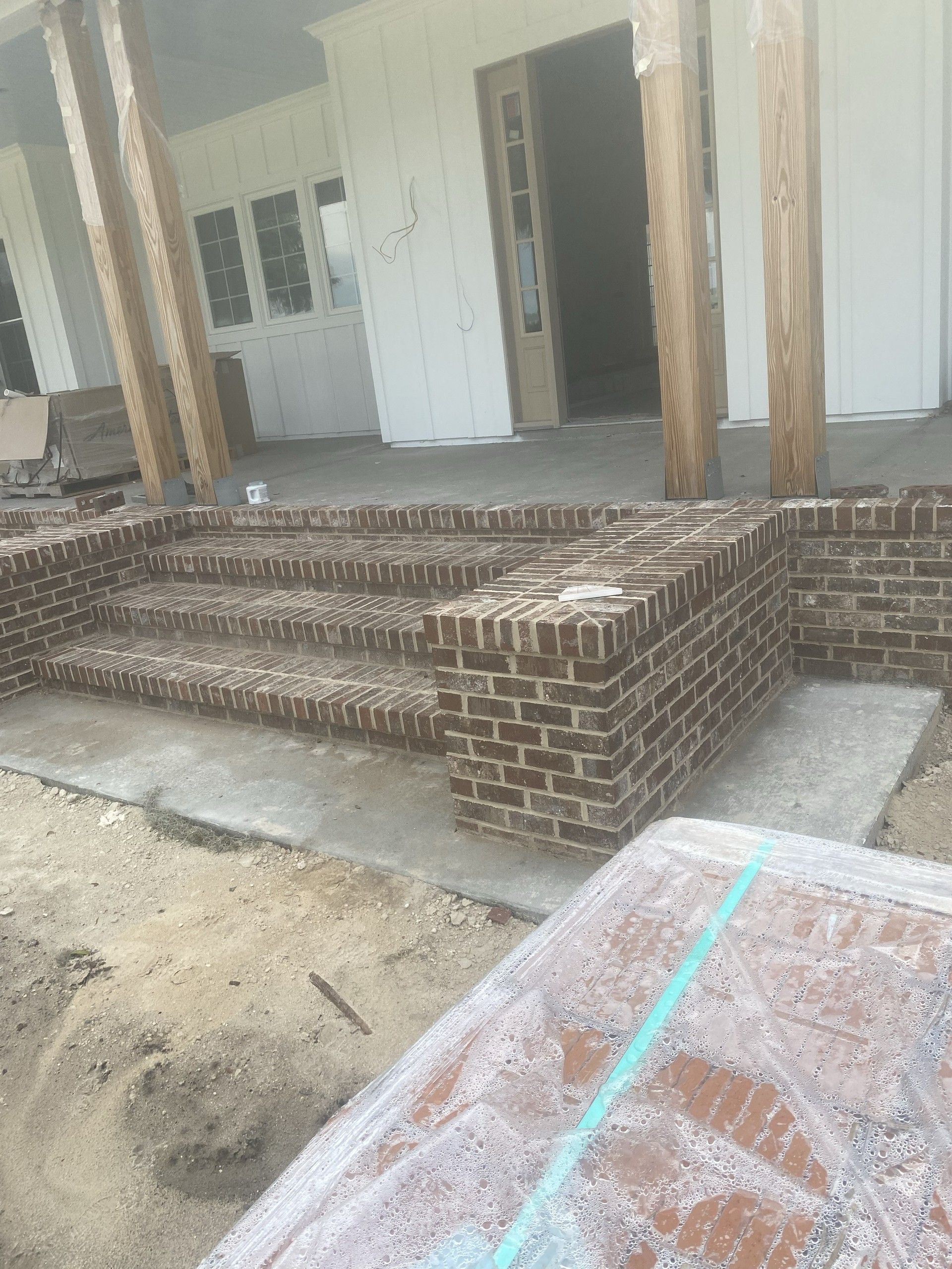 Brick entry steps and a low brick wall in front of a covered porch, with a plastic-covered pallet of bricks in the foreground