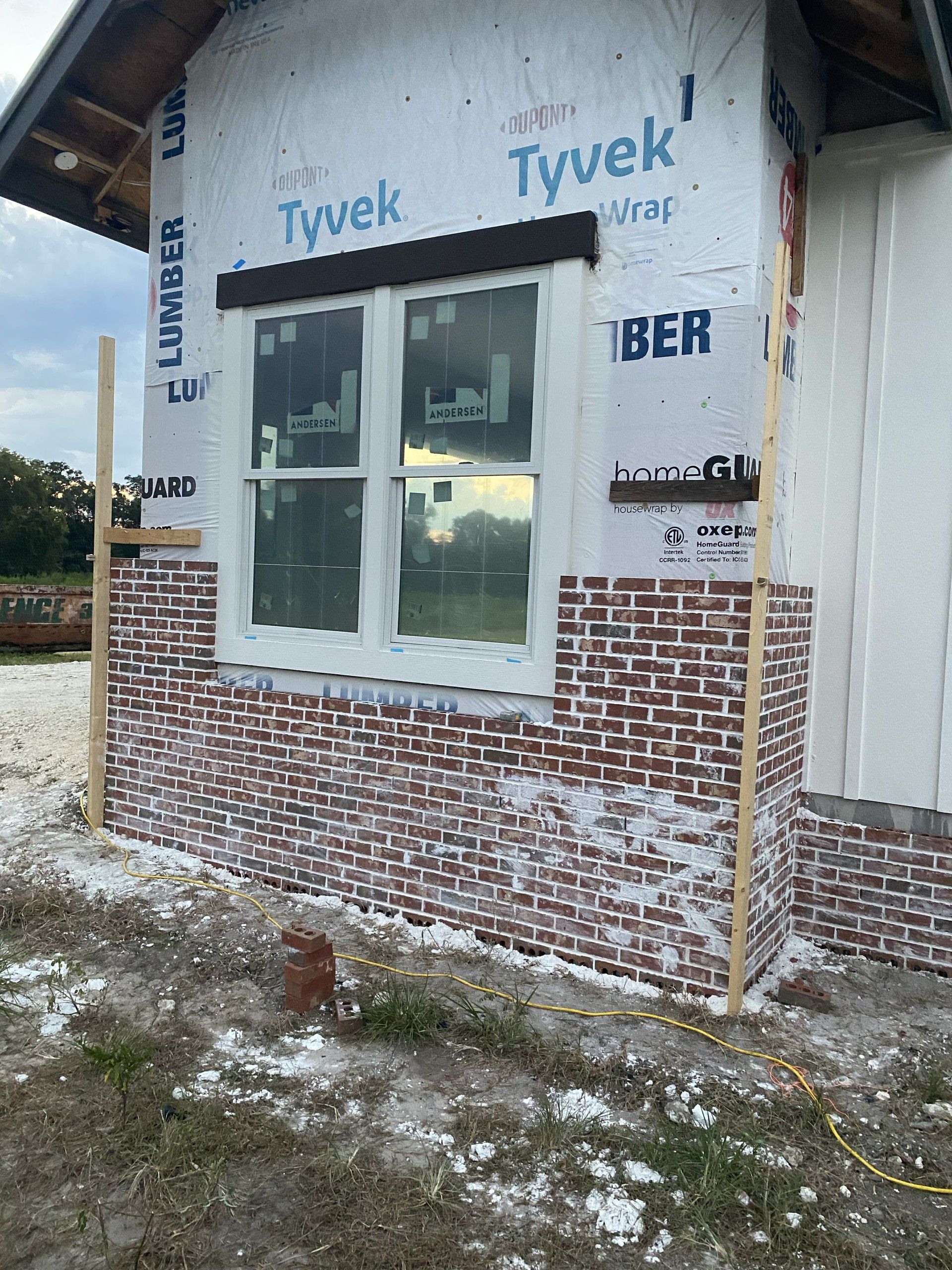 Brick veneer laid partway up a wall covered in printed housewrap, surrounding a white double-hung window