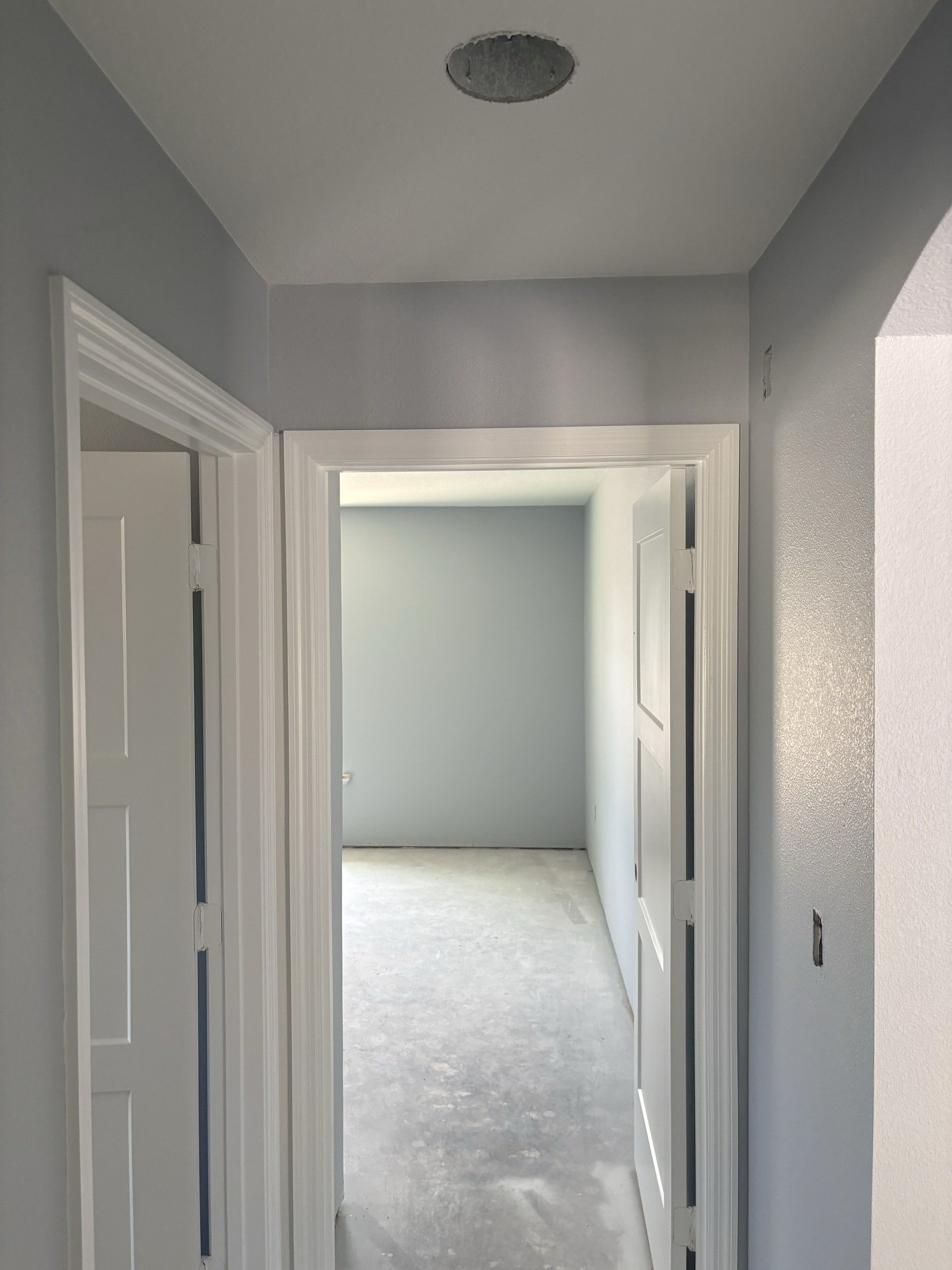 Hallway with white trimmed doorways and panel doors opening into an empty bedroom with a bare concrete floor