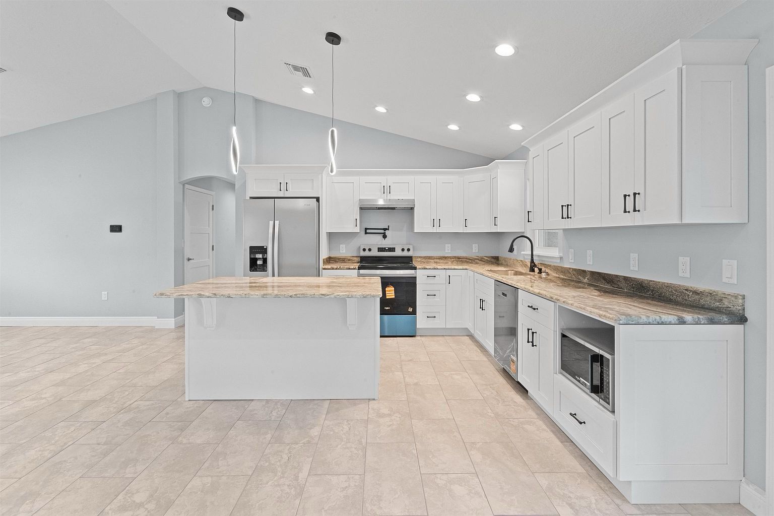 Kitchen with a long run of white shaker cabinets, granite countertops, built-in microwave, dishwasher, and a large island with two pendant lights above